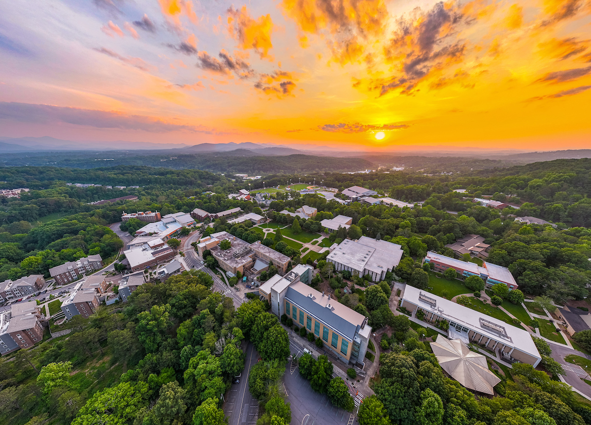 Drone image of UNCA campus and sunset behind mountains