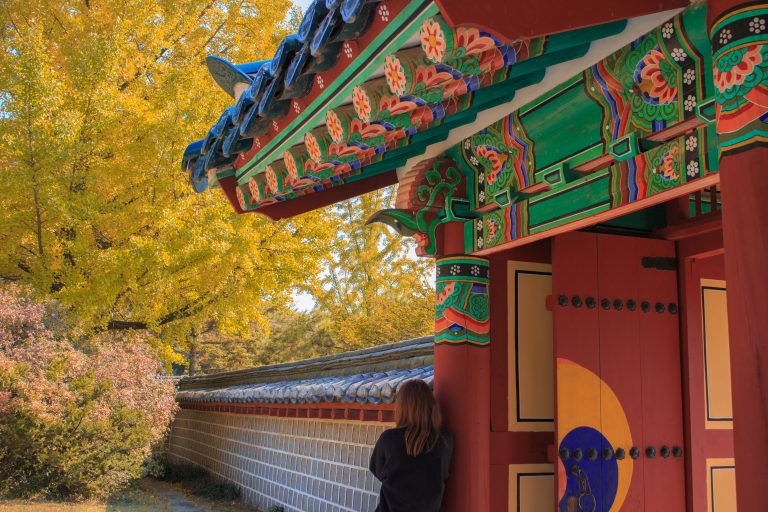 A student leaning against the wall of a traditional style building in Korea