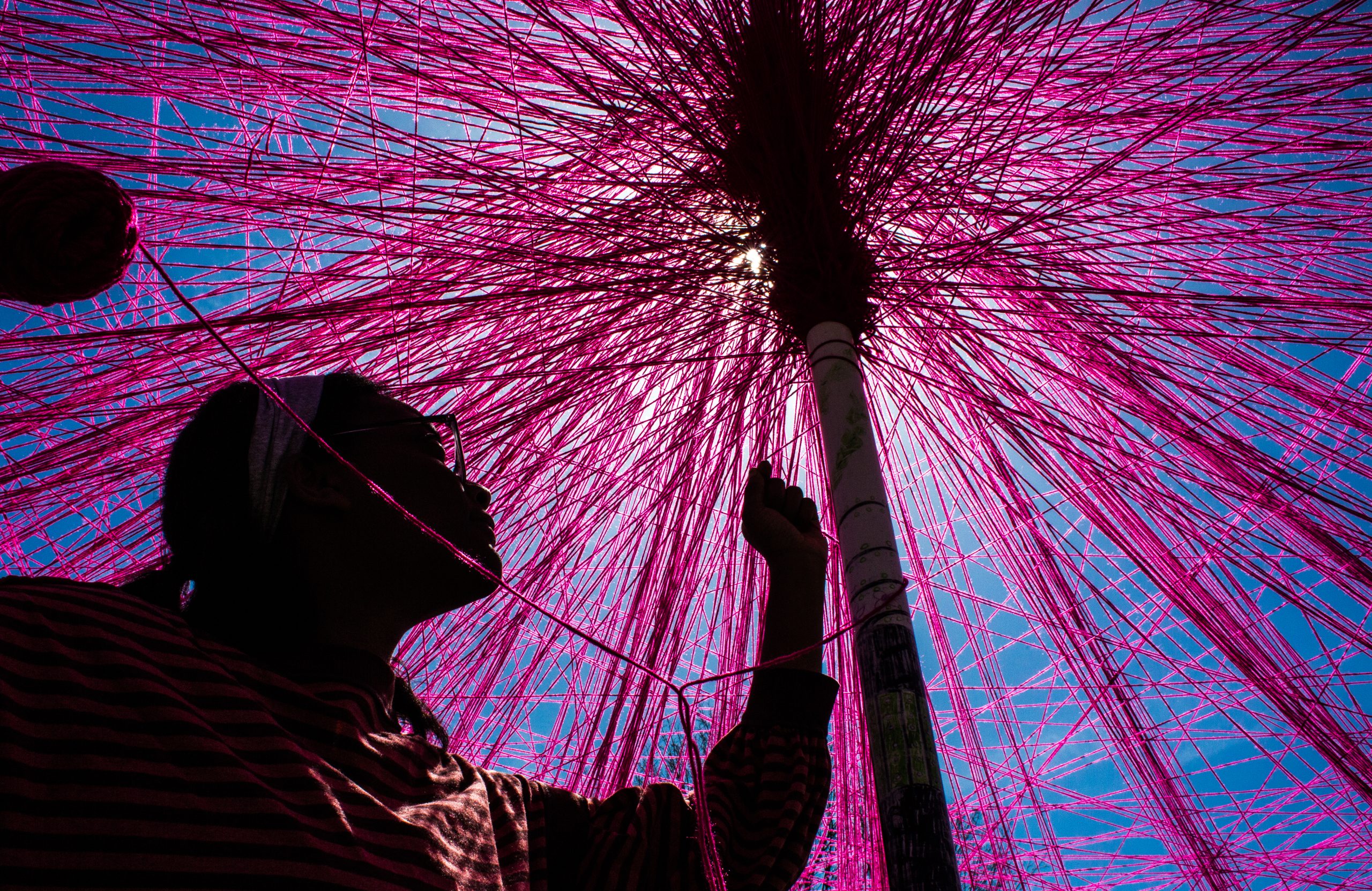 A person working on an installation art piece made of pink threads
