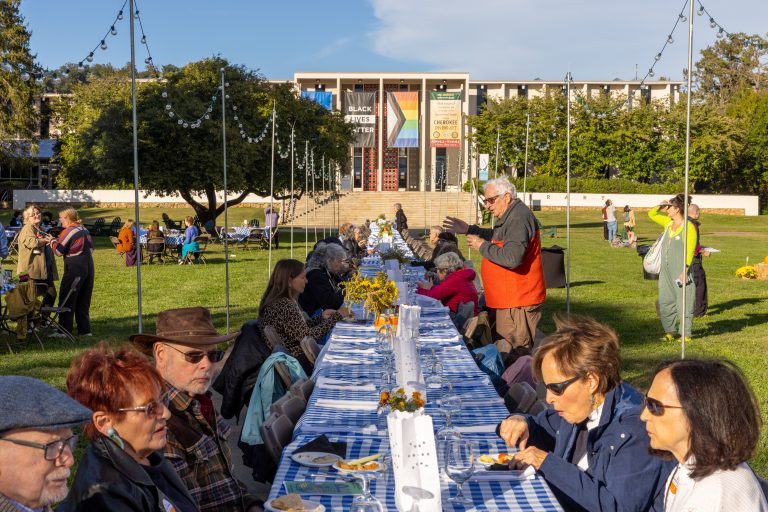 People sitting at a long table on the quad, with Ramsey Library in the background