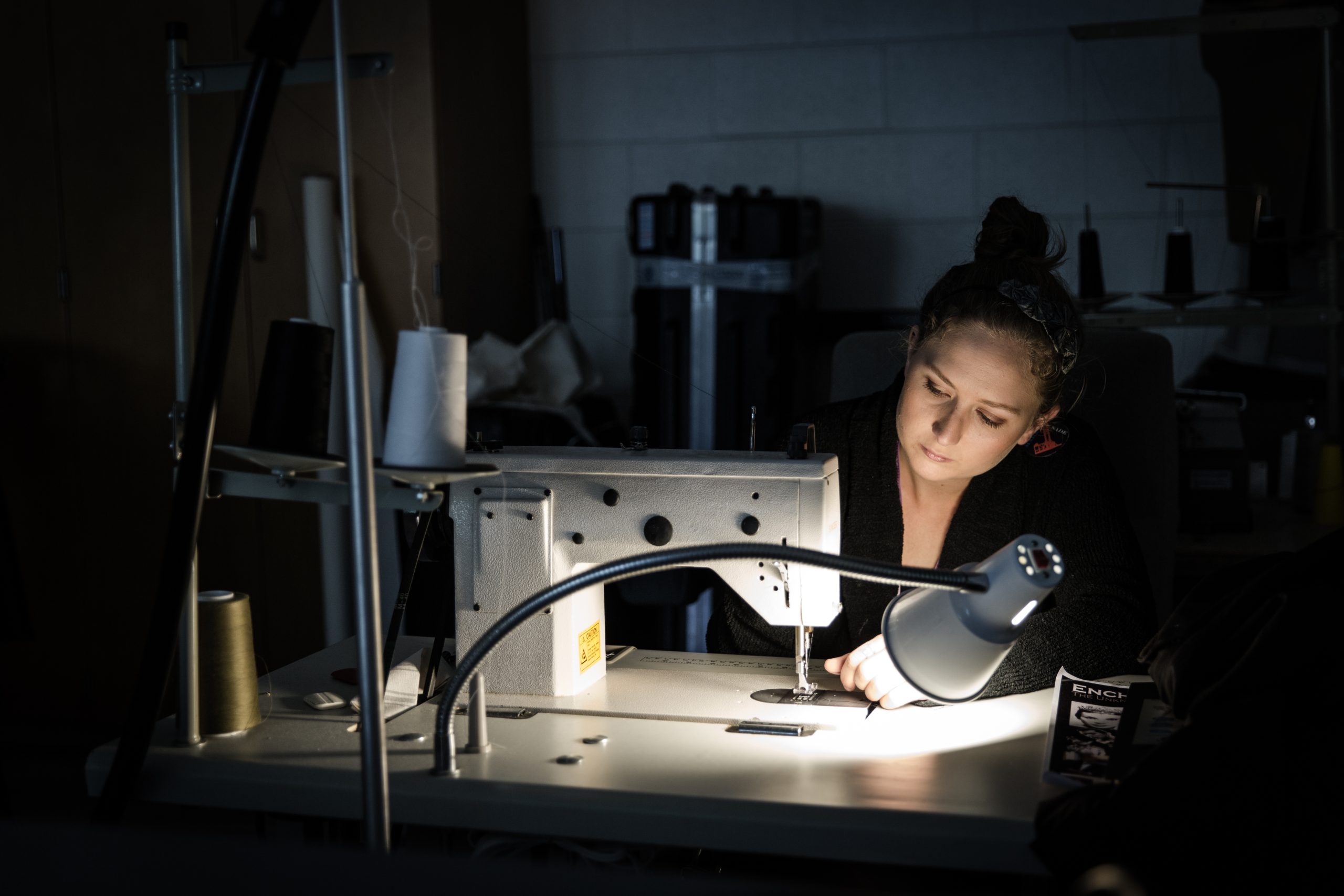 Drama student using a sewing machine in a dark room