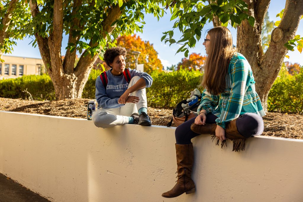 Two students sit near a walkway by ramsey library talking to each other