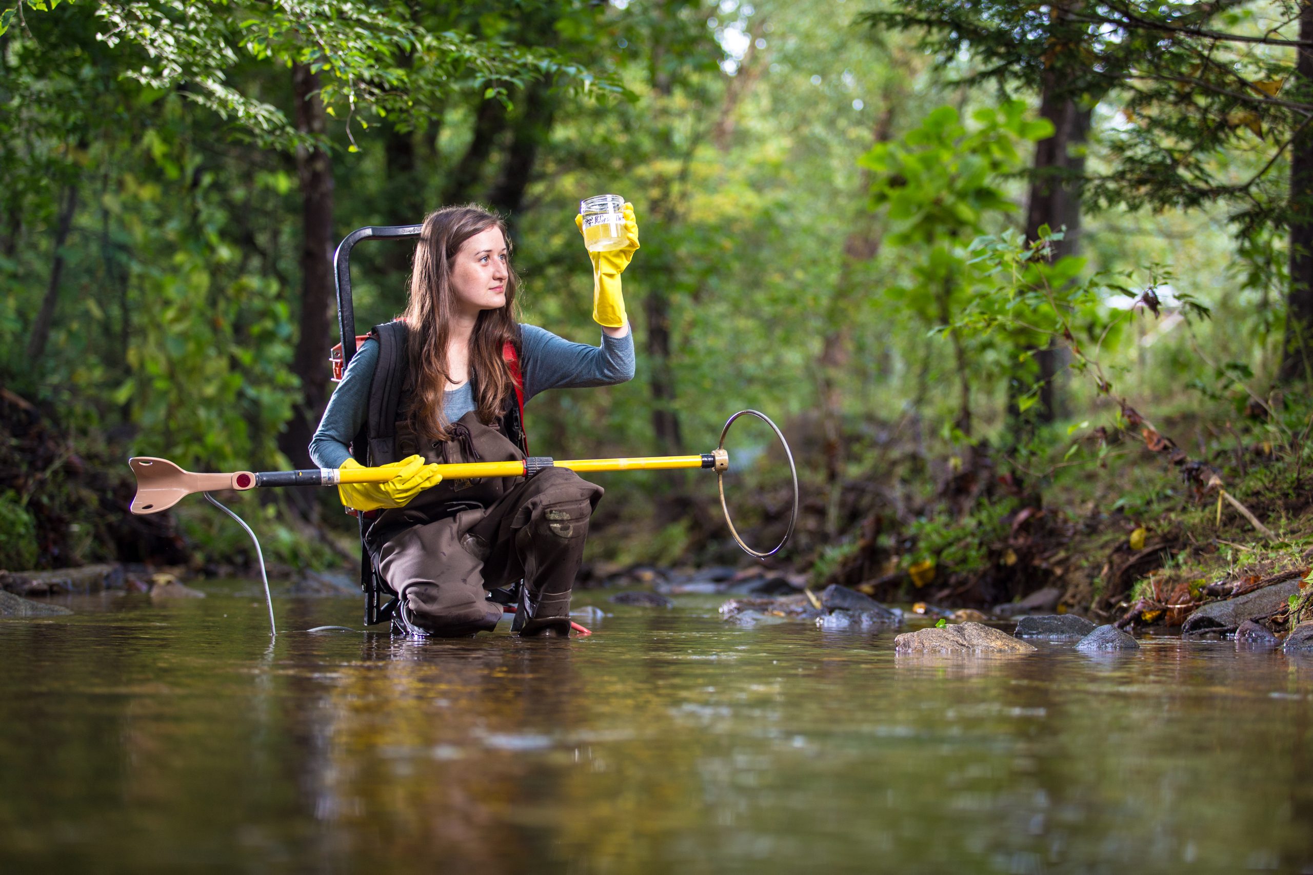 Someome standing in a river with research equipment, examining a water sample