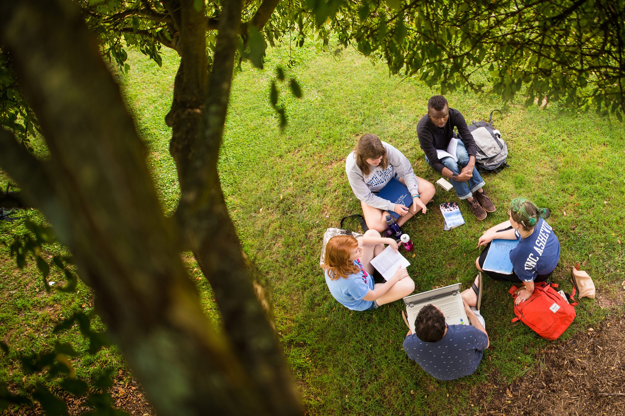 overhead shot of five students sitting on the grass in a circle