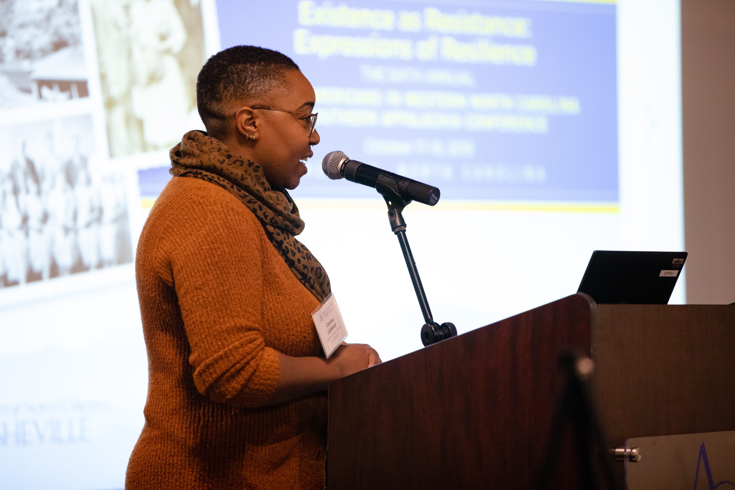 a speaker at a conference standing at a podium with a powerpoint presentation in the background