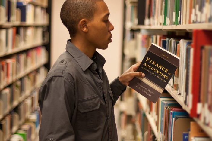 Someone taking a finance book of a library book shelf