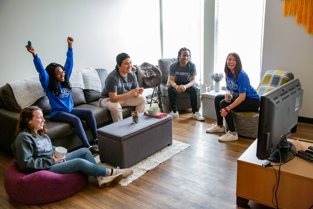 A group of people sitting in a woods apartment common area playing a video game