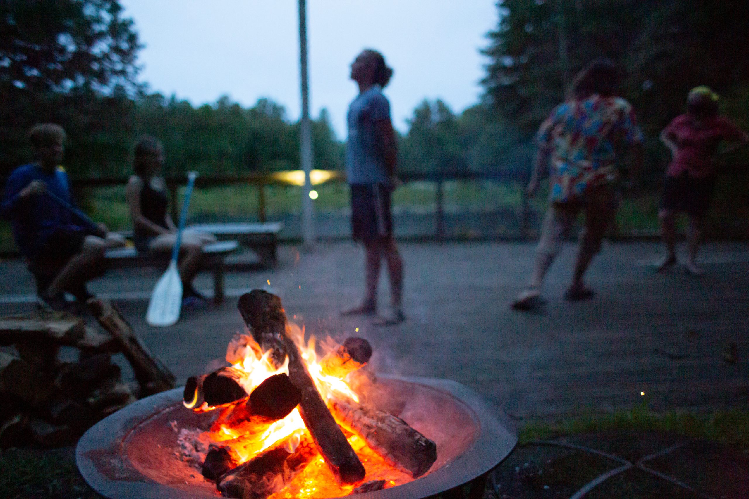 Some people gathered by a fire pit at dusk