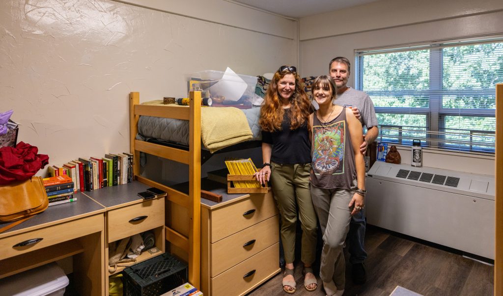 Student and parents standing in residence hall room unpacking during August 2023 Move-In.