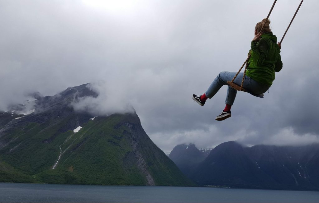 A student swinging above the water near a large mountain in Norway