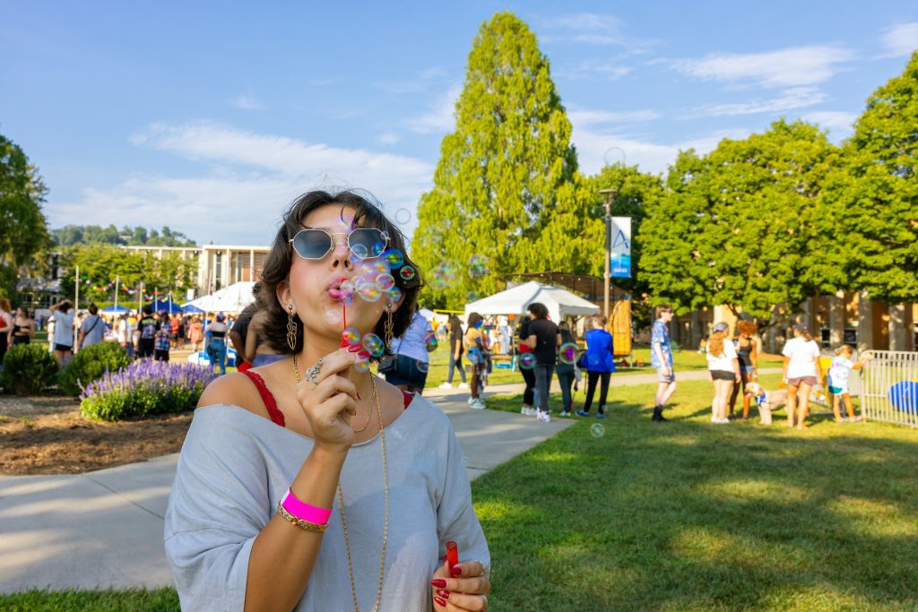 A student blowing bubbles at rockypalooza on the quad with other students behind them