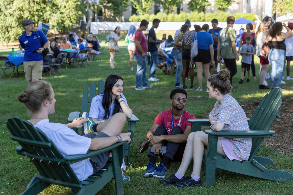 four people sitting on the quad together with many more students in the background