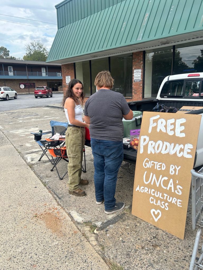 Environmental student Emma Carr with fresh produce loaded in a truck, next ti a sign reading 'Free produce gifted by UNCA's agriculture class