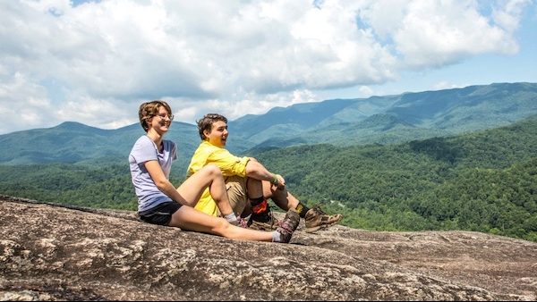 two students sitting on an exposed rock in the mountains